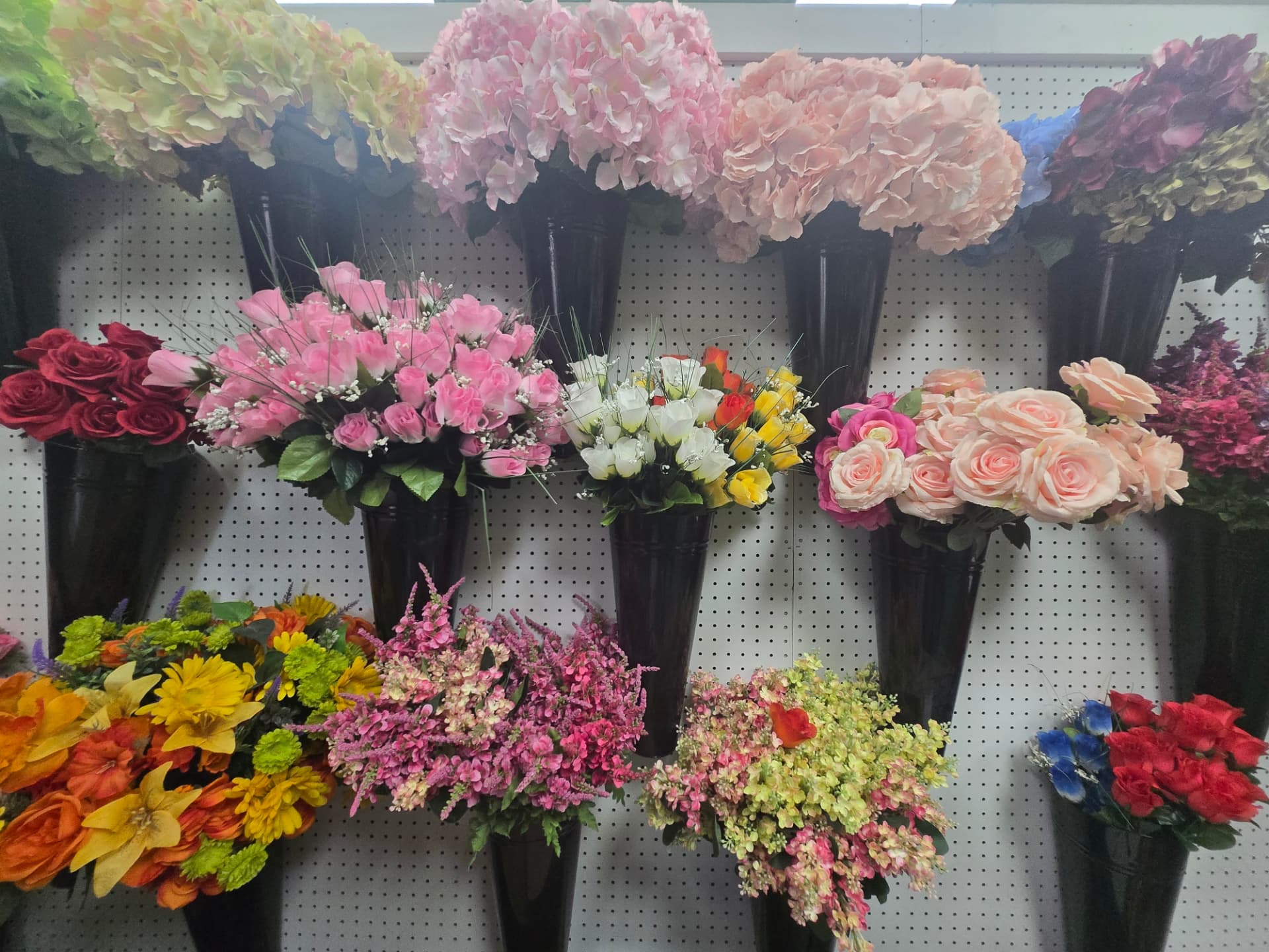Wall of silk flower bunches in black florist buckets — hydrangeas, roses and blossom stems