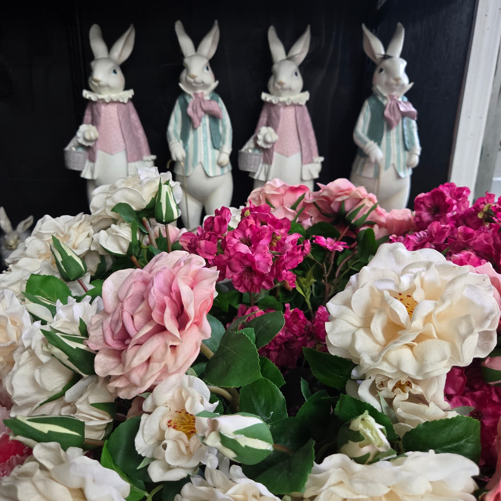 Silk roses and geraniums in front of dressed ceramic Easter bunnies